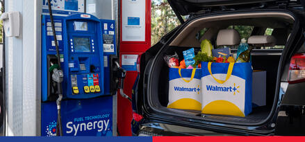 An open car trunk at an Exxon fuel pump. Inside the open trunk are two Walmart bags full of groceries.