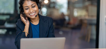 Smiling customer service representative sitting in front of a laptop and wearing a headset