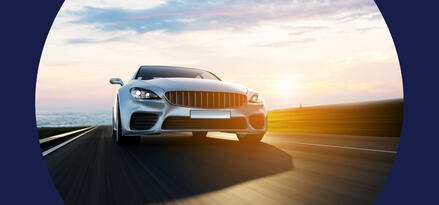 A car is driving down the open highway just before sunset with a glow behind it and heavenly looking clouds