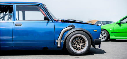 Card showing old-school blue car with a green car in the bakcground, likely at a car show or gathering.