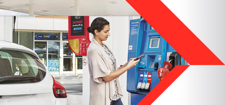 A brunette woman at an Exxon gas pump, holding her phone in her hands to access the Exxon Mobil Rewards+ app
