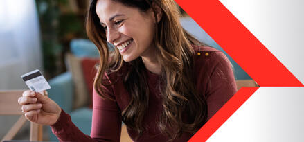 A woman sitting in front of a laptop smiling and looking at a gift card