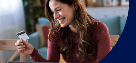 A woman sitting in front of a laptop smiling and looking at a gift cardRewards+