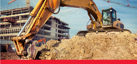 A large yellow excavator lifting dirt at and an active construction site. There is a partially built building int he background with text: Construction