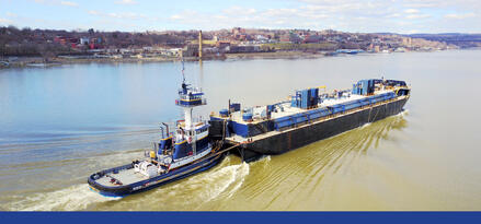 A long industrial barge traveling on calm inland water with text: Inland marine