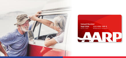An older man wearing a floppy fishing hat is smiling and leaning on a truck to talk to an older woman through the window with a graphic of an AARP member card placed next to them.