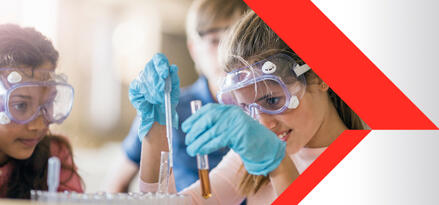 Two young students in a classroom using a pipette to transfer liquids between test tubes