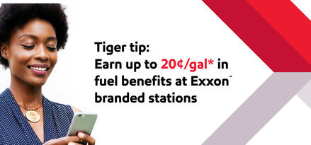 A woman holding a smart phone and smiling as she looks at it, with text: Tiger tip: Earn up to 20¢/gal* in fuel benefits at Exxon™ branded stations.