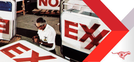 A slightly grainy image from the Exxon archives of an older man in glasses working on Exxon branded station signage.