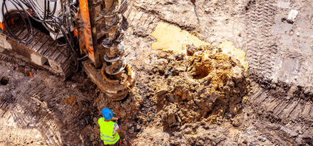 A man in a hard hat and yellow vest next to an oil drill is a gas field.