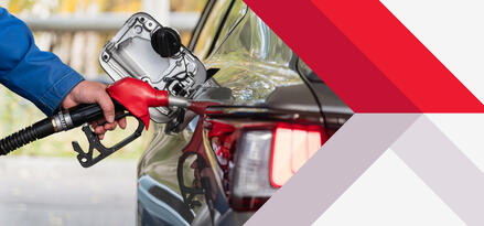 A hand holding a red gas nozzle as it fills up a car.