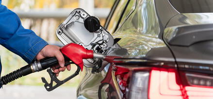 A hand holding a red gas nozzle as it fills up a car.