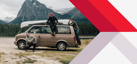 Three men standing on or around a brown van with a canoe strapped to the top in a mountainous area