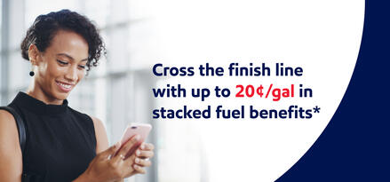 A woman smiling at her smart phone with text: Cross the finish line with up to 20¢/gal in stacked fuel benefits*