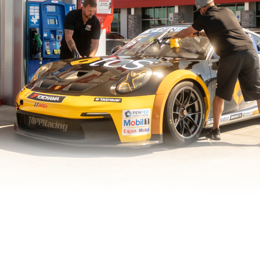 A Mobil-branded Porsche race car at the gas station pump with two men cleaning the car's windshield.