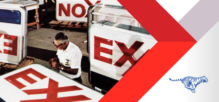 A slightly grainy image from the Exxon archives of an older man in glasses working on Exxon branded station signage.