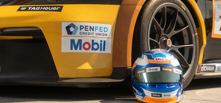 Close up of front bumper of yellow Porsche Carrera race car with helmet on ground in front of tire.