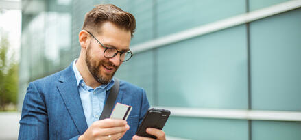 A man holding a gift card while looking at his mobil phone